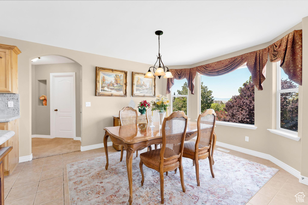 Dining space featuring light tile patterned floors, a chandelier, and arched walkways