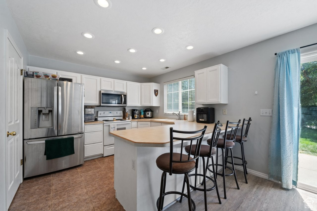 Kitchen with appliances with stainless steel finishes, a peninsula, recessed lighting, plenty of natural light, and white cabinets