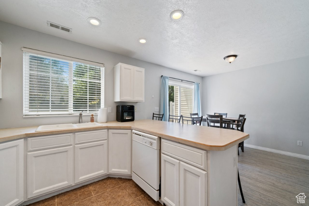Kitchen featuring white dishwasher, a peninsula, healthy amount of natural light, recessed lighting, and white cabinets