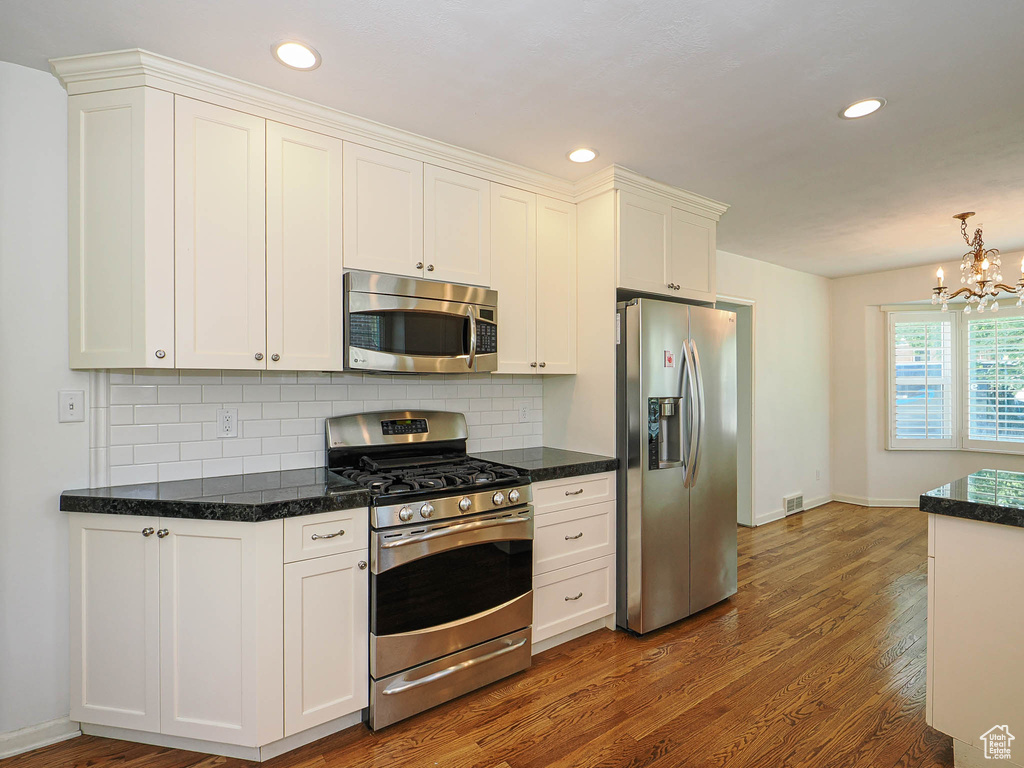 Kitchen featuring stainless steel appliances, wood finished floors, backsplash, white cabinets, and recessed lighting