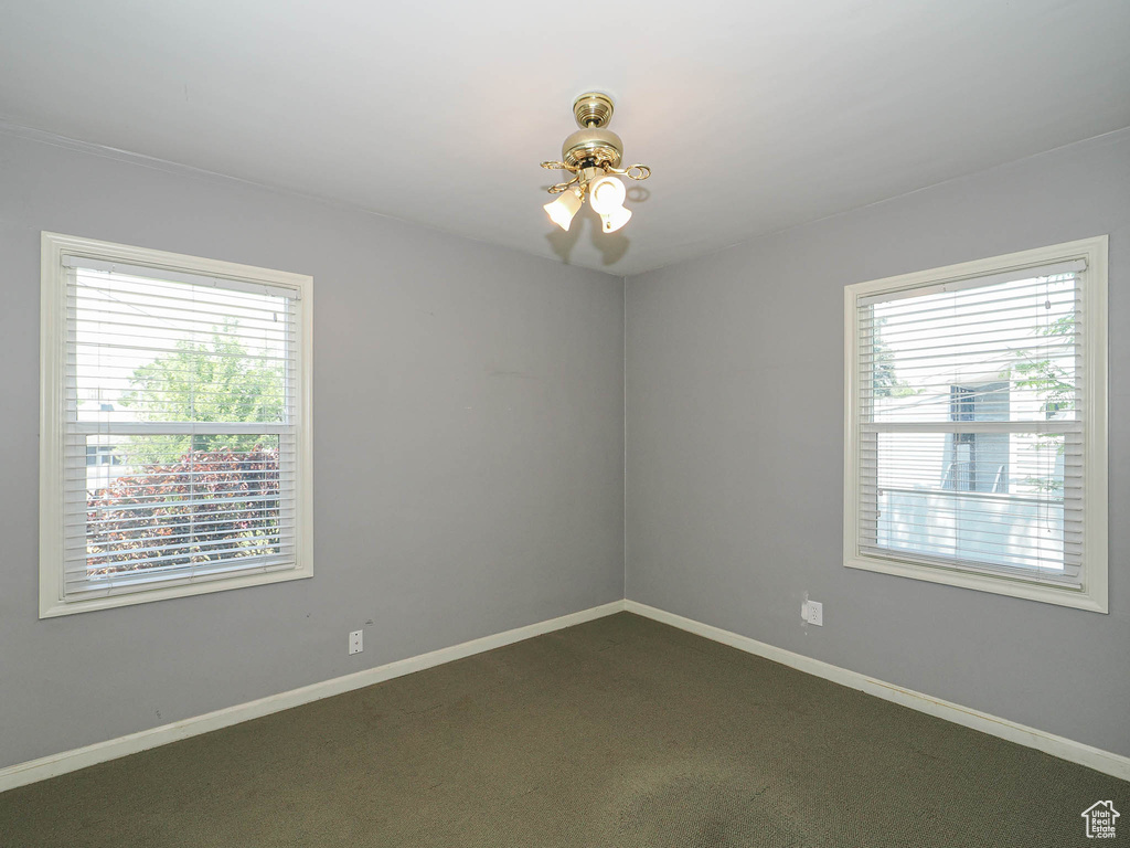 Unfurnished room featuring healthy amount of natural light, dark colored carpet, and a ceiling fan