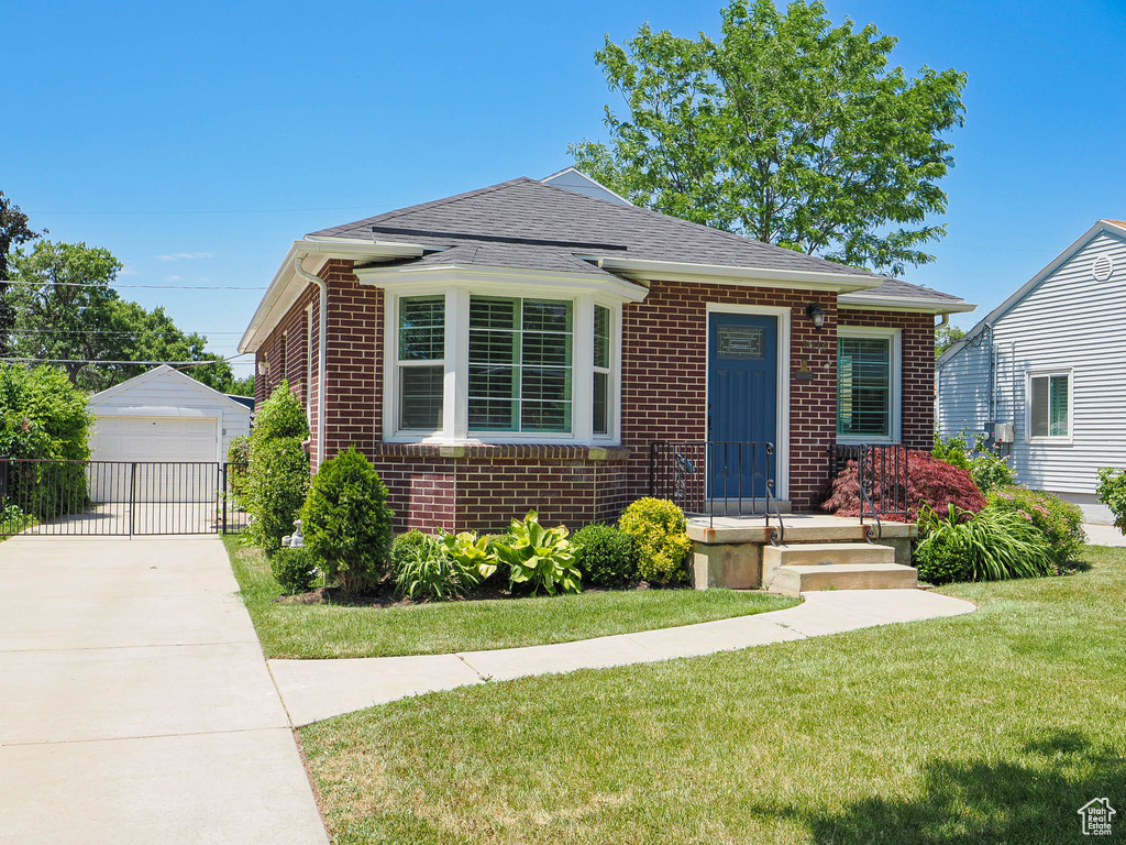 Bungalow with brick siding, a front lawn, an outbuilding, a shingled roof, and a garage