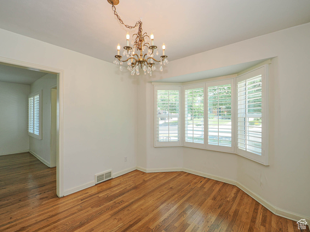 Empty room with plenty of natural light, a chandelier, and wood finished floors