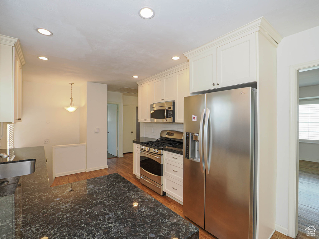 Kitchen featuring stainless steel appliances, decorative backsplash, white cabinetry, wood finished floors, and recessed lighting