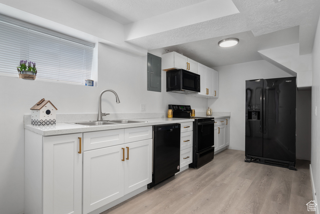 Kitchen with black appliances, a textured ceiling, electric panel, light wood finished floors, and white cabinets