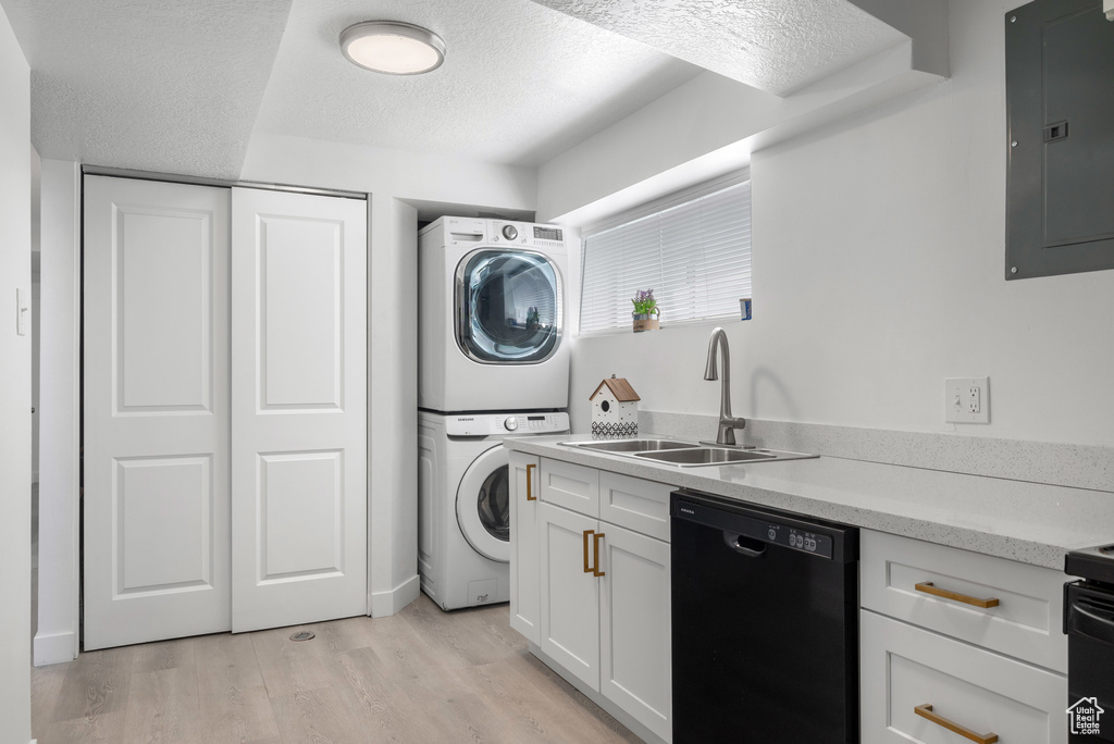 Laundry room featuring stacked washer / dryer, electric panel, light wood-style flooring, and a textured ceiling
