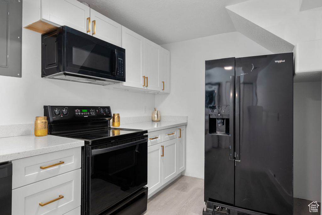 Kitchen with black appliances, white cabinetry, light wood-style floors, and light stone countertops