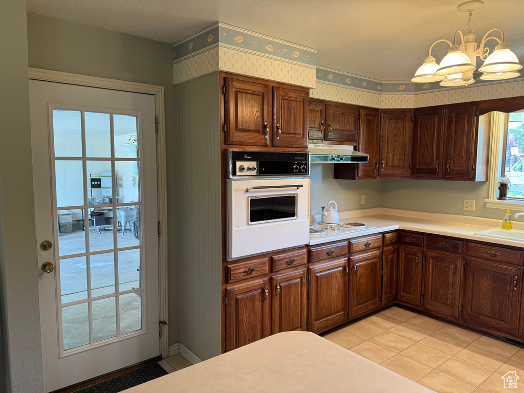 Kitchen featuring white appliances, under cabinet range hood, a chandelier, light countertops, and light tile patterned floors