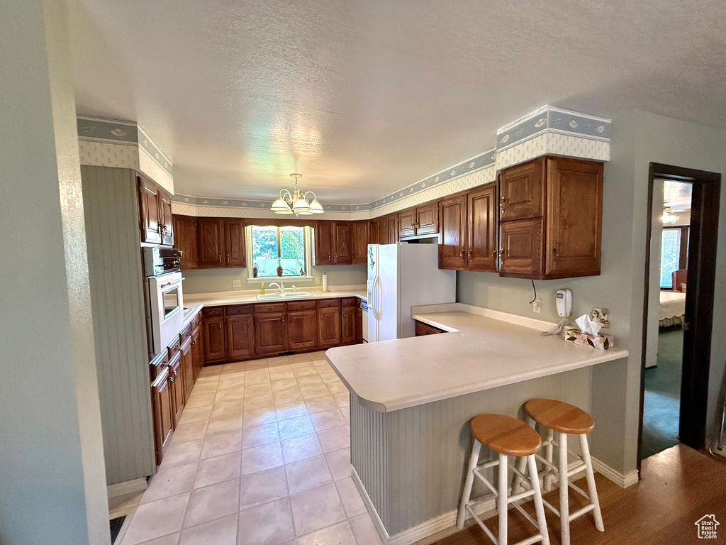 Kitchen with white appliances, a peninsula, a chandelier, light countertops, and a textured ceiling