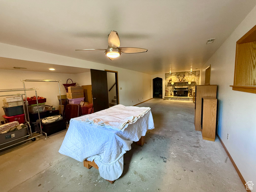 Bedroom featuring concrete flooring, a stone fireplace, and a ceiling fan