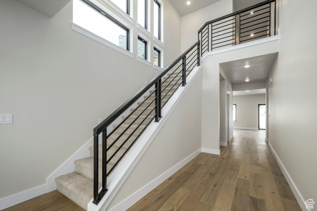 Stairway featuring wood finished floors, baseboards, a high ceiling, and recessed lighting