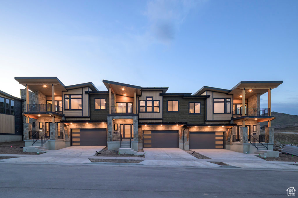 Contemporary house featuring a balcony, a garage, driveway, and stone siding