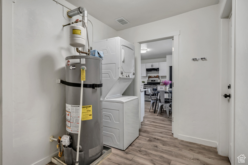 Laundry area featuring stacked washer / drying machine, water heater, and light wood finished floors
