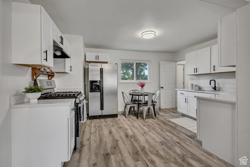 Kitchen with appliances with stainless steel finishes, under cabinet range hood, light countertops, and white cabinetry