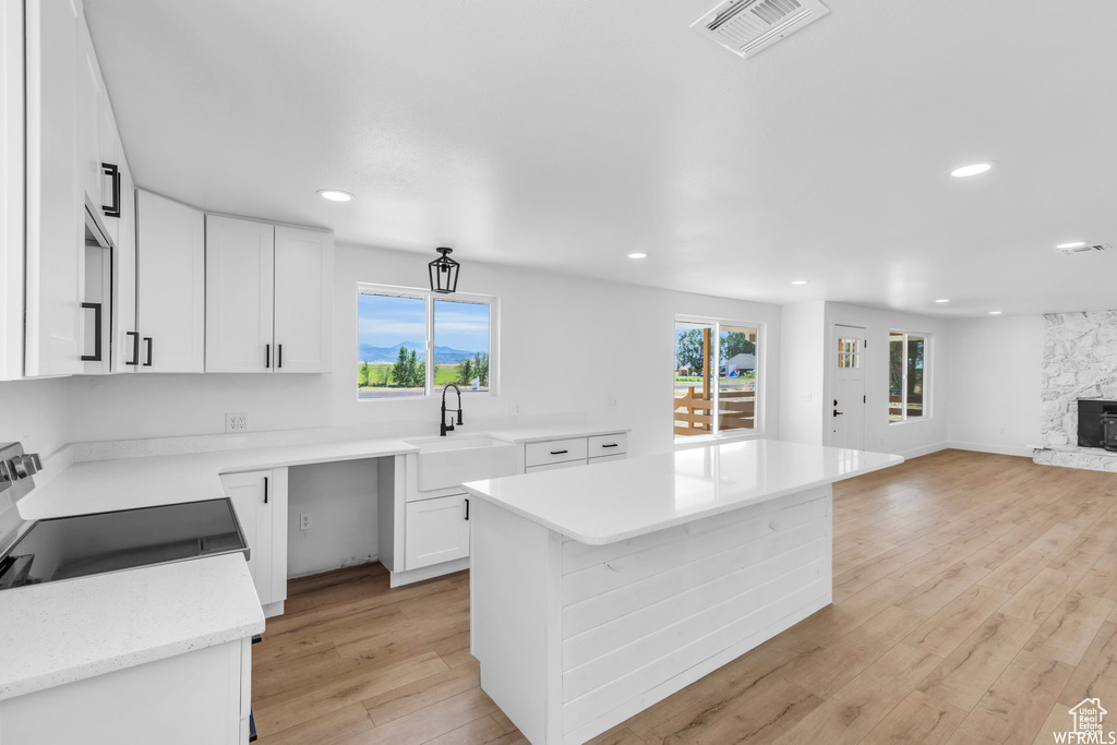 Kitchen with electric range oven, recessed lighting, white cabinets, light wood-type flooring, and a kitchen island