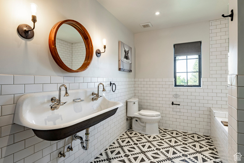Bathroom featuring tile walls, tile patterned flooring, tiled tub, and a wainscoted wall