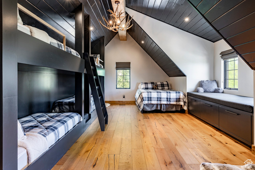 Bedroom with a chandelier, light wood finished floors, wooden ceiling, multiple windows, and vaulted ceiling