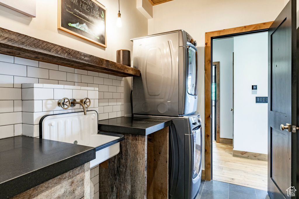 Washroom with stacked washing machine and dryer and dark tile patterned floors