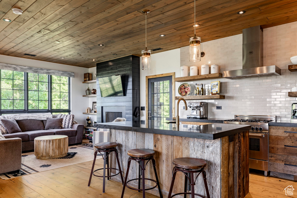 Kitchen featuring high end range, island exhaust hood, dark countertops, light wood finished floors, and a breakfast bar area