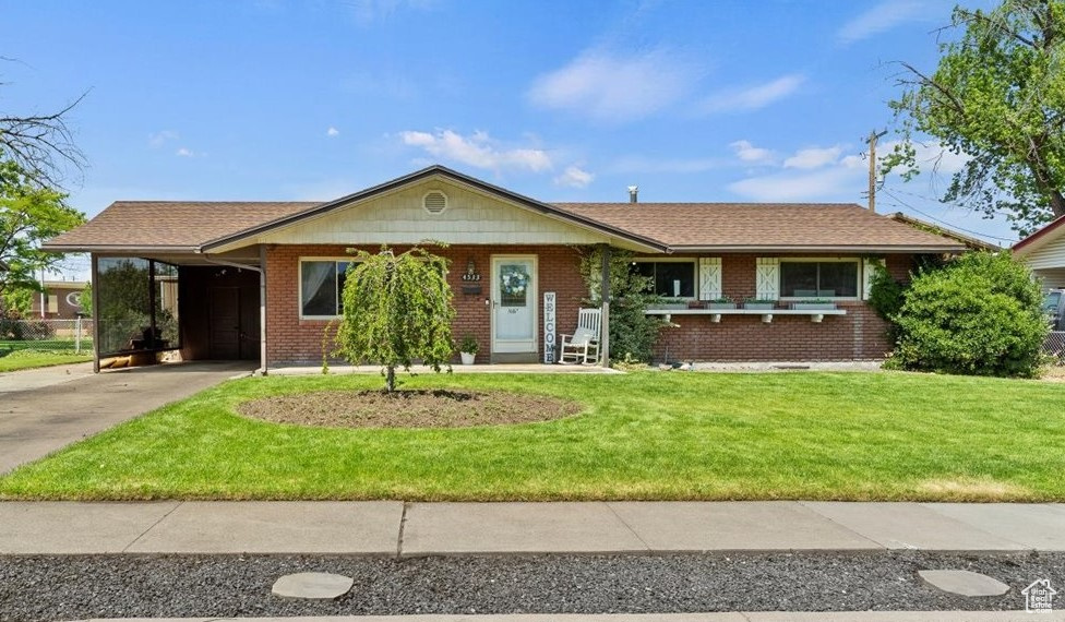 View of front of home featuring driveway, a carport, a front yard, and brick siding
