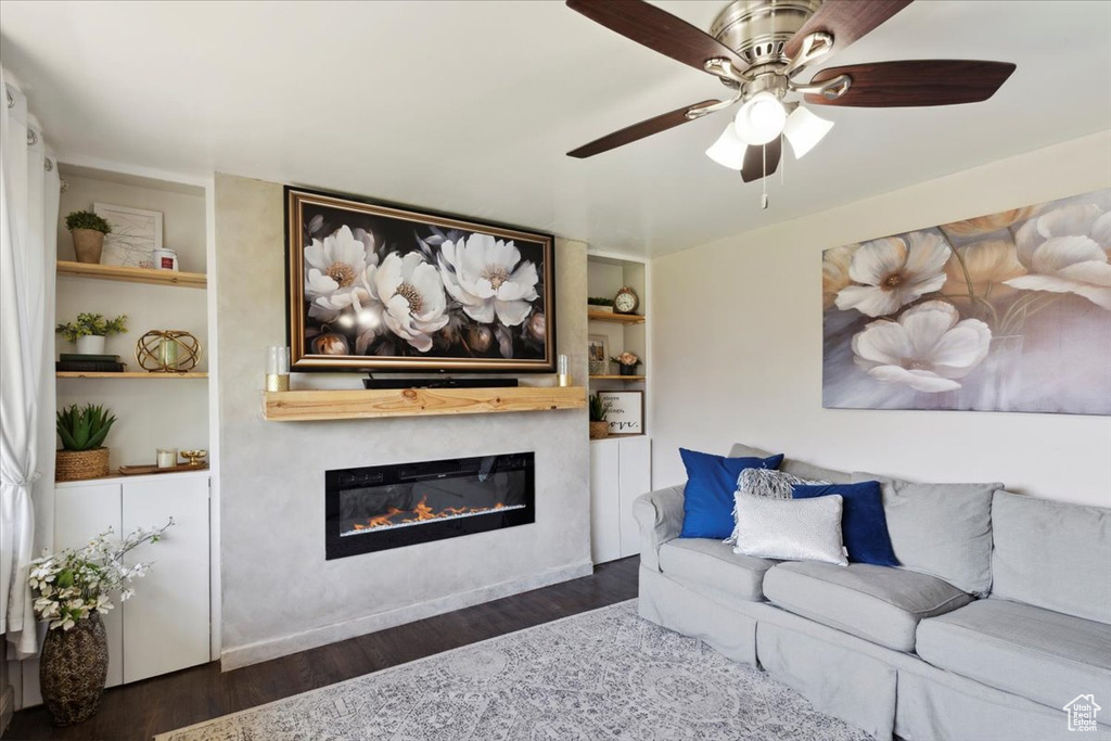 Living room with a glass covered fireplace, wood finished floors, a ceiling fan, and built in features