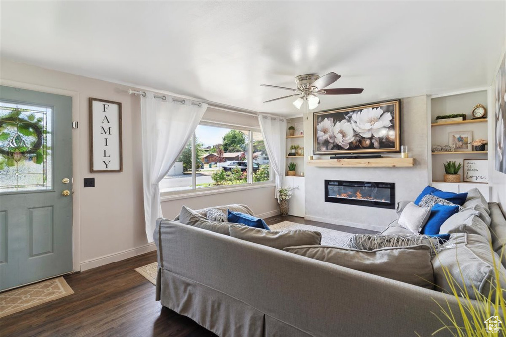 Living area with healthy amount of natural light, a glass covered fireplace, ceiling fan, and dark wood-type flooring