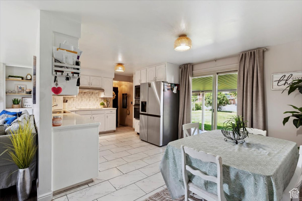 Kitchen featuring appliances with stainless steel finishes, white cabinets, light countertops, decorative backsplash, and light marble finish floors