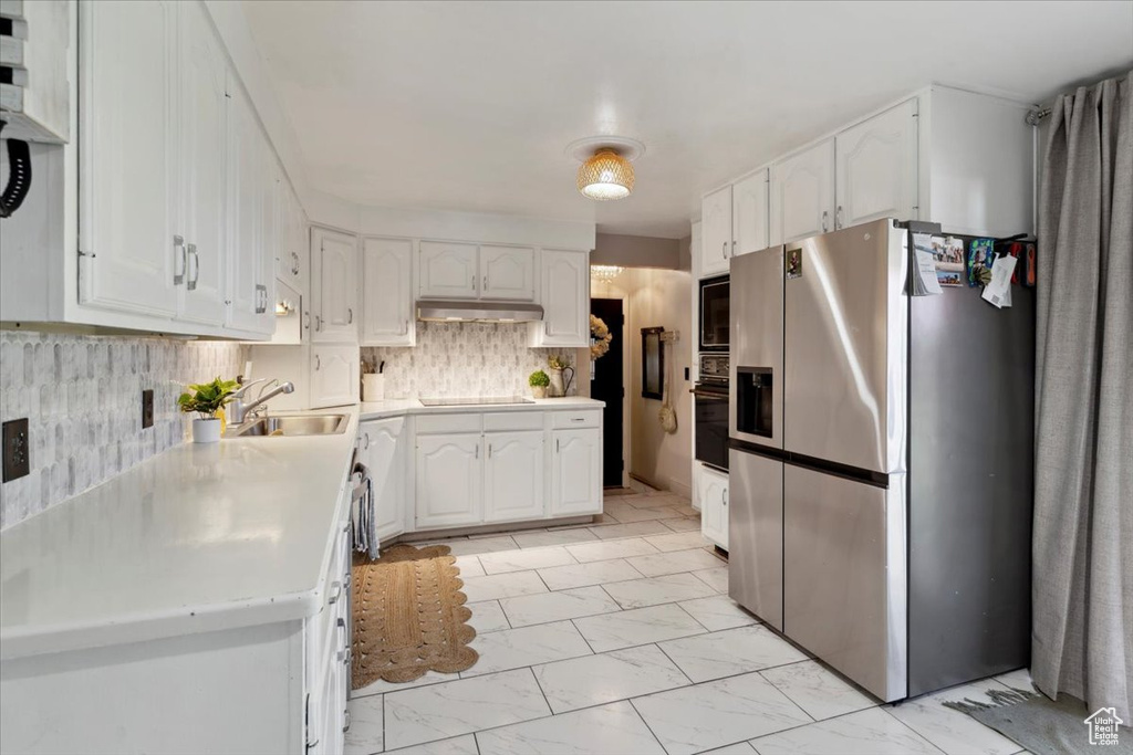 Kitchen with black appliances, light marble finish floors, white cabinetry, and under cabinet range hood