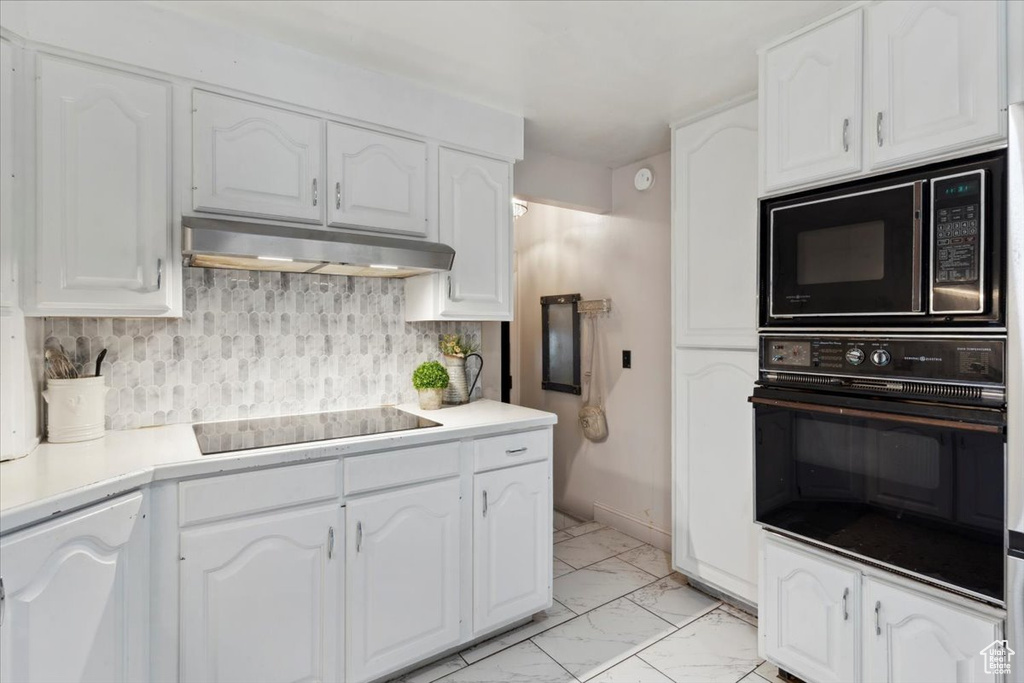 Kitchen with black appliances, under cabinet range hood, light marble finish flooring, and white cabinetry