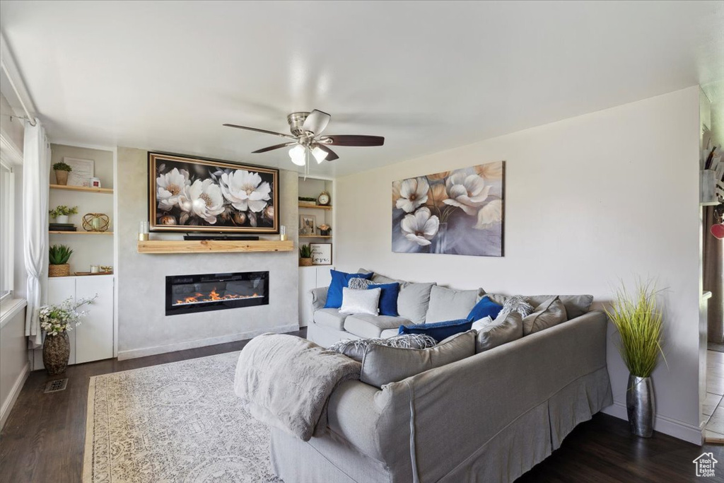 Living area featuring ceiling fan, dark wood-style floors, a glass covered fireplace, and built in features