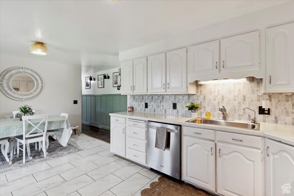 Kitchen with stainless steel dishwasher, white cabinetry, light countertops, light marble finish floors, and backsplash