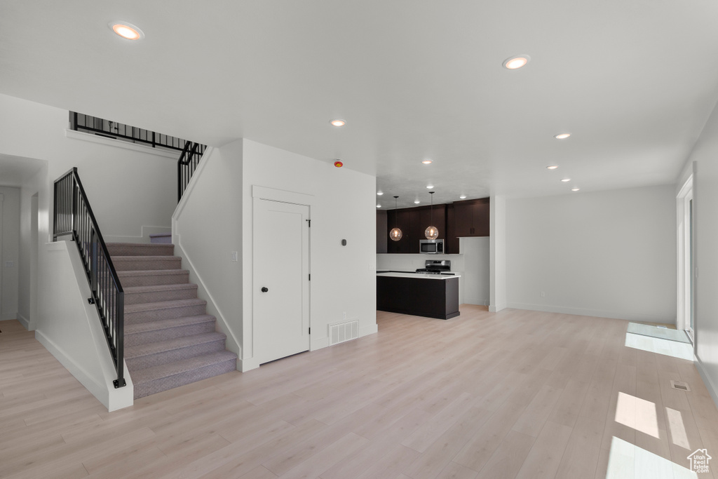 Unfurnished living room featuring stairs, light wood finished floors, and recessed lighting