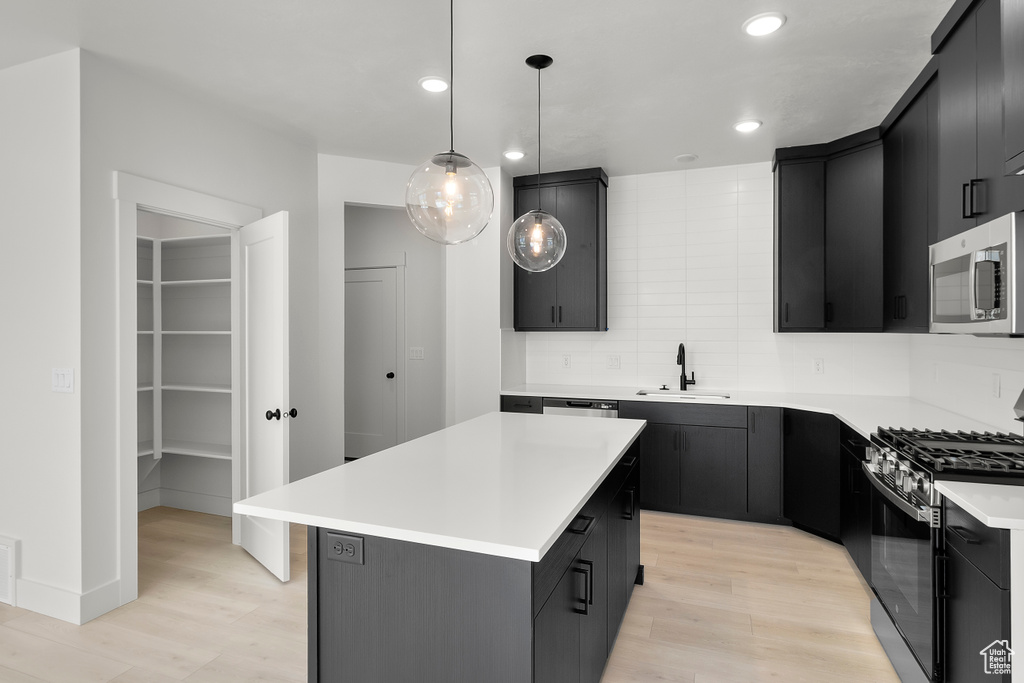 Kitchen featuring stainless steel appliances, dark cabinetry, light wood-style flooring, and recessed lighting
