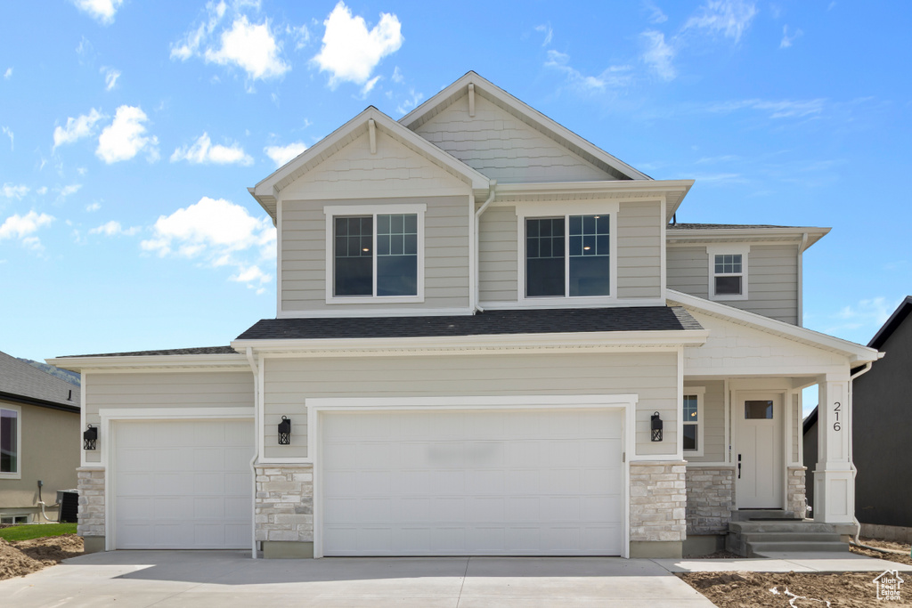 Craftsman-style home featuring stone siding, driveway, and a garage