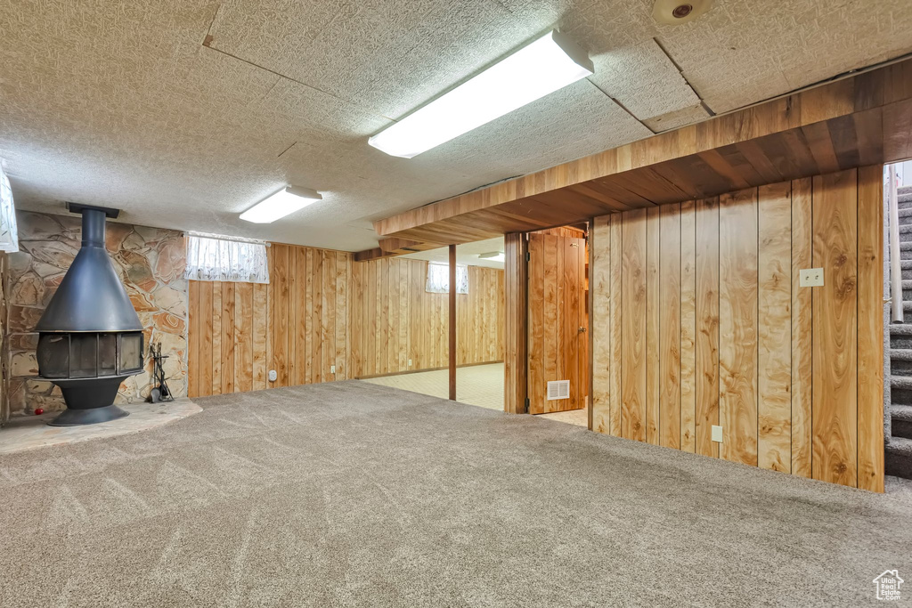 Basement with wood walls, carpet, stairs, and a wood stove