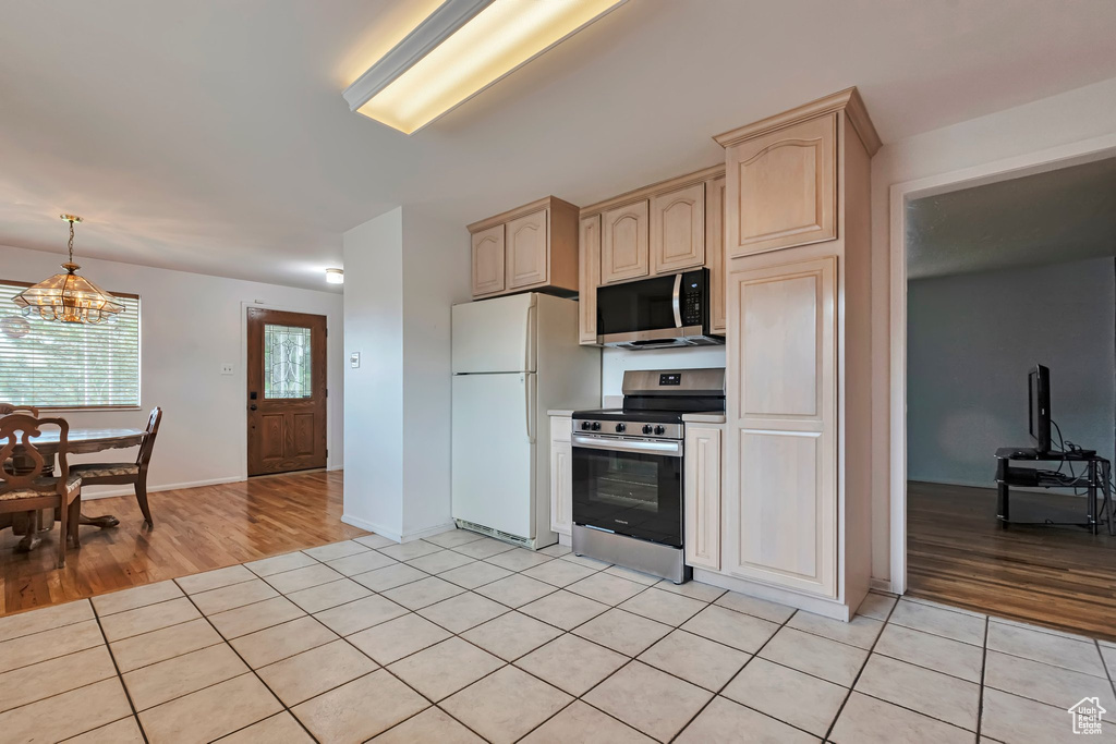 Kitchen with stainless steel appliances, light tile patterned floors, light brown cabinetry, hanging light fixtures, and a chandelier