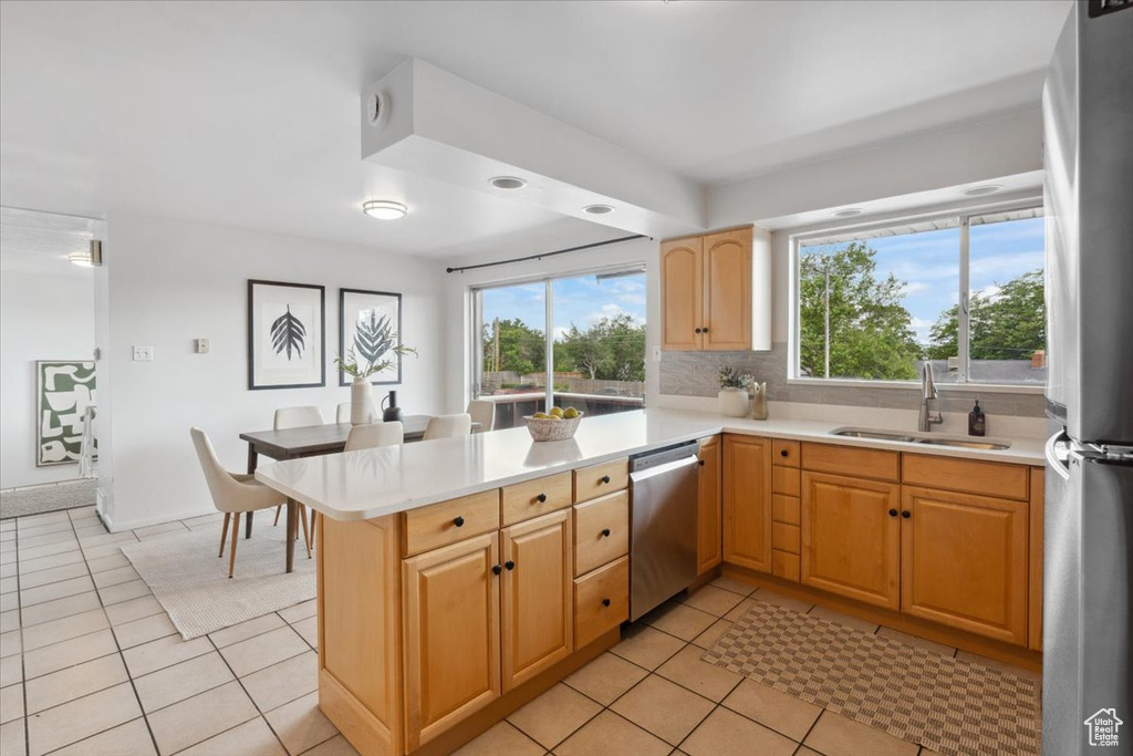 Kitchen with appliances with stainless steel finishes, light tile patterned floors, light countertops, a peninsula, and healthy amount of natural light