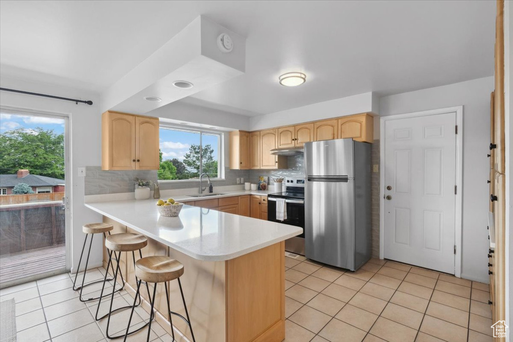 Kitchen with stainless steel appliances, light brown cabinets, a peninsula, and under cabinet range hood