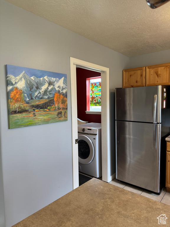 Washroom featuring washer / dryer, light tile patterned floors, and a textured ceiling