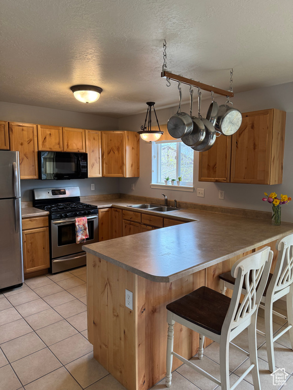 Kitchen featuring stainless steel appliances, a peninsula, a breakfast bar, light tile patterned floors, and a textured ceiling