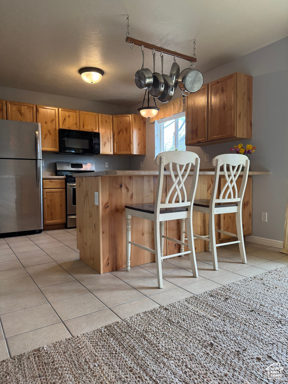 Kitchen featuring stainless steel appliances, a peninsula, light tile patterned floors, a kitchen breakfast bar, and a textured ceiling