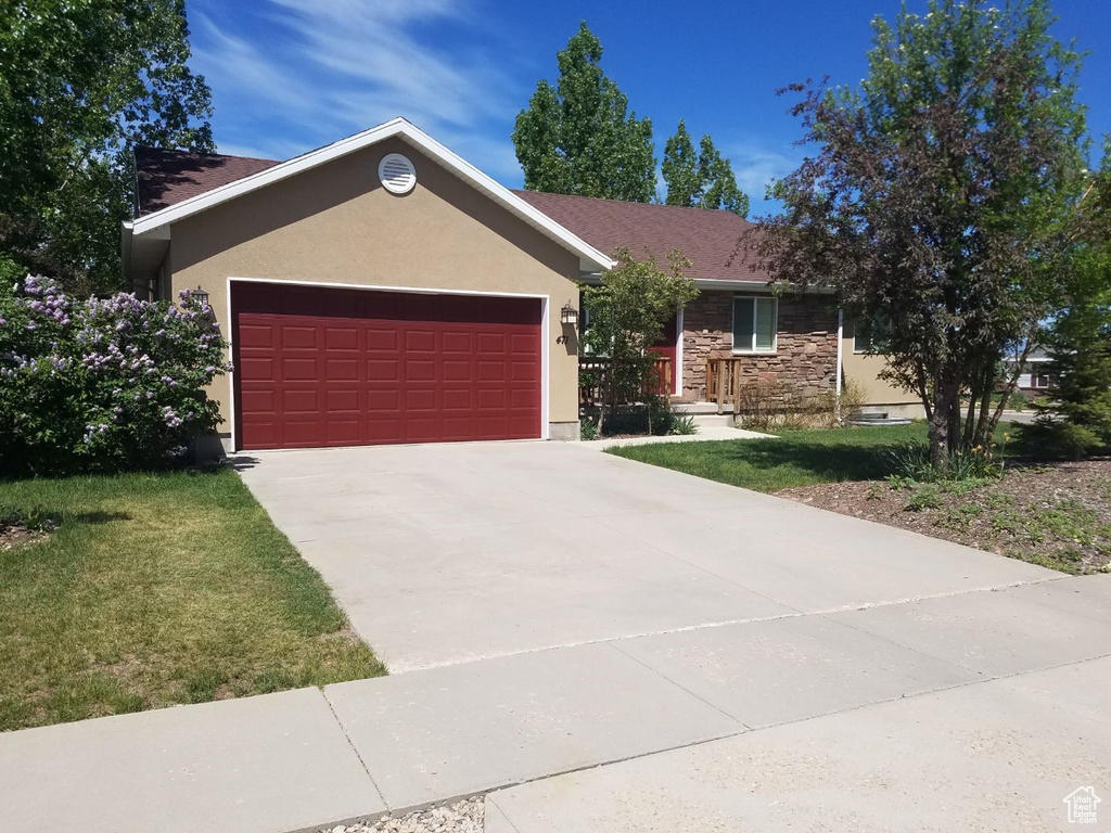 Single story home with stucco siding, a garage, stone siding, driveway, and a front yard