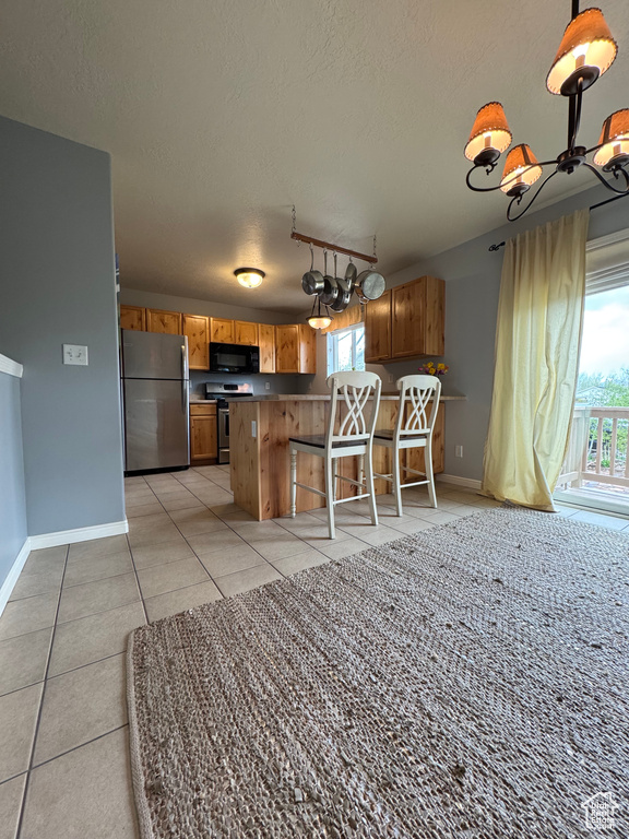 Kitchen featuring appliances with stainless steel finishes, a chandelier, brown cabinets, a textured ceiling, and light tile patterned flooring
