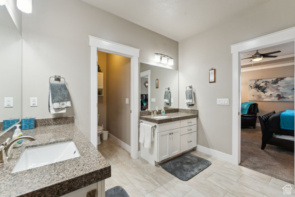 Bathroom featuring two vanities, ensuite bathroom, a ceiling fan, toilet, and baseboards