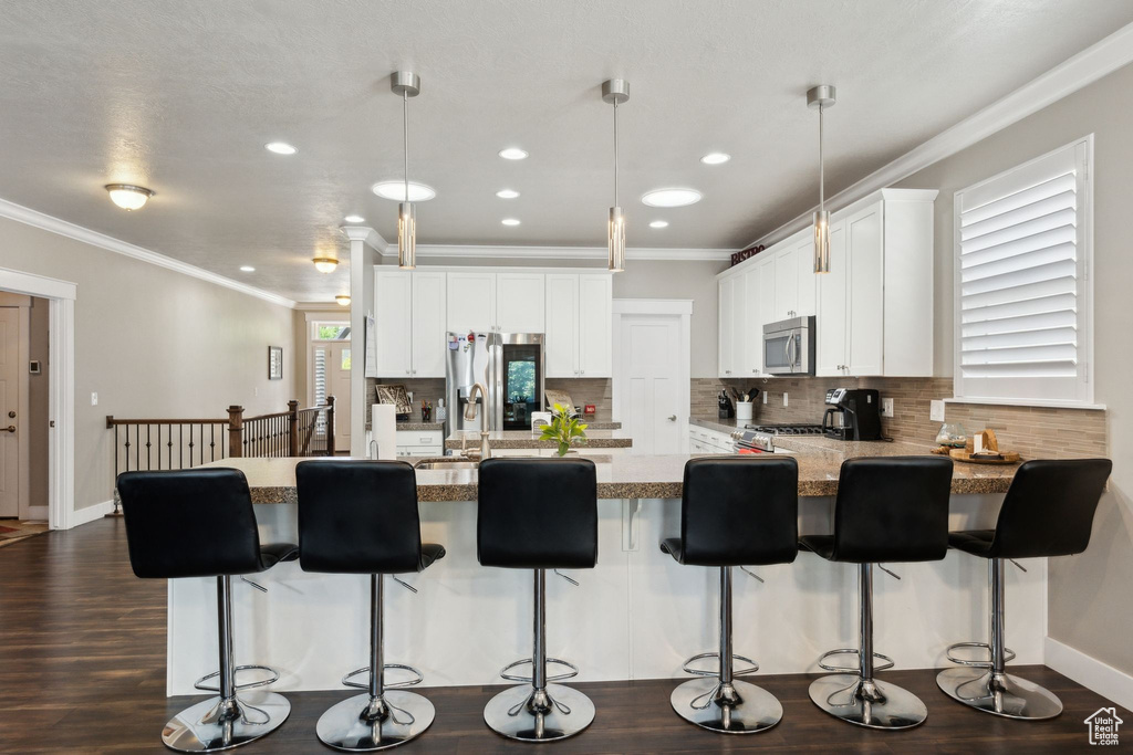 Kitchen with appliances with stainless steel finishes, tasteful backsplash, a peninsula, crown molding, and white cabinetry
