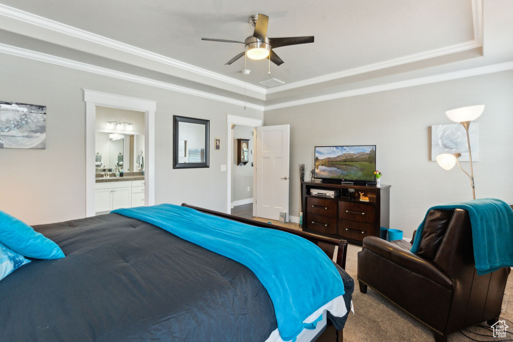 Carpeted bedroom featuring a tray ceiling, ornamental molding, connected bathroom, and a ceiling fan