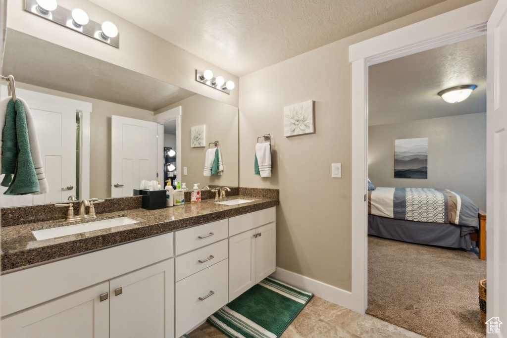 Ensuite bathroom with double vanity, baseboards, and a textured ceiling