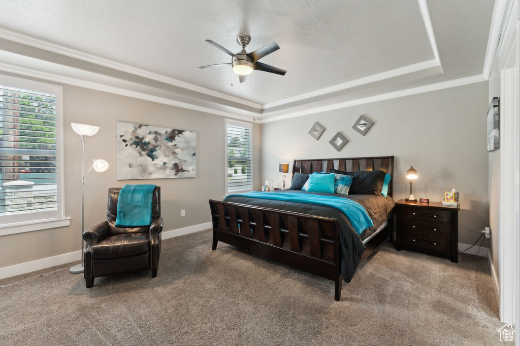 Bedroom featuring a tray ceiling, baseboards, light carpet, ornamental molding, and a ceiling fan