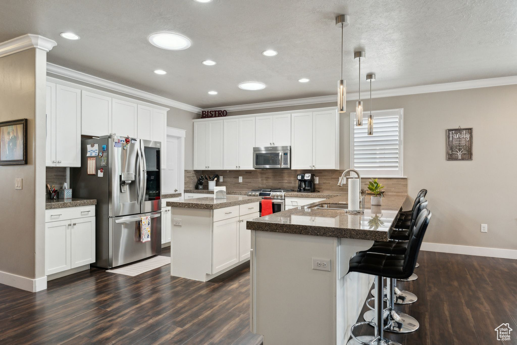 Kitchen with appliances with stainless steel finishes, a sink, dark wood-style flooring, ornamental molding, and a peninsula
