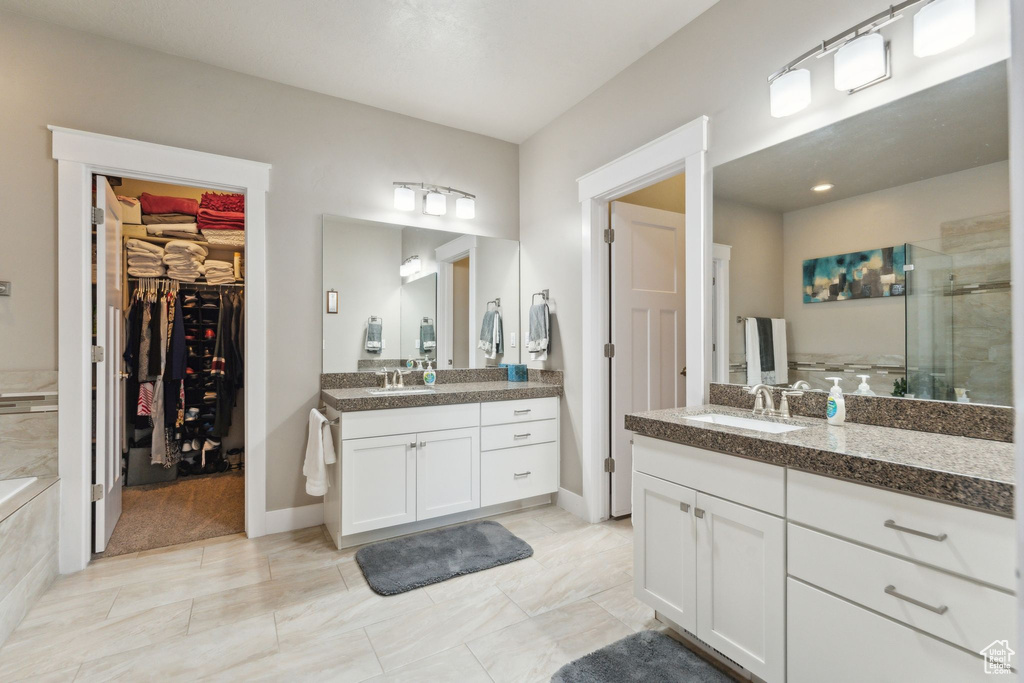 Bathroom featuring a stall shower, two vanities, a spacious closet, and baseboards